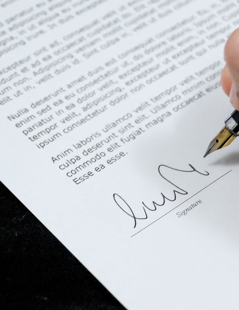Close-up of a hand signing a formal document with a fountain pen, indicating agreement.